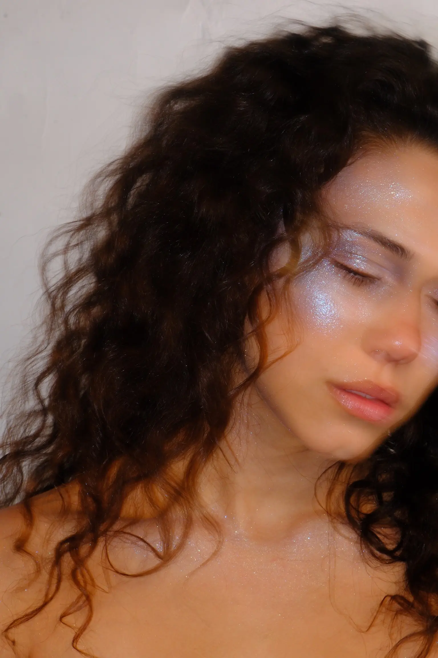 Close portrait of Bella Valdes, eyes closed, curls falling across her face in soft light.